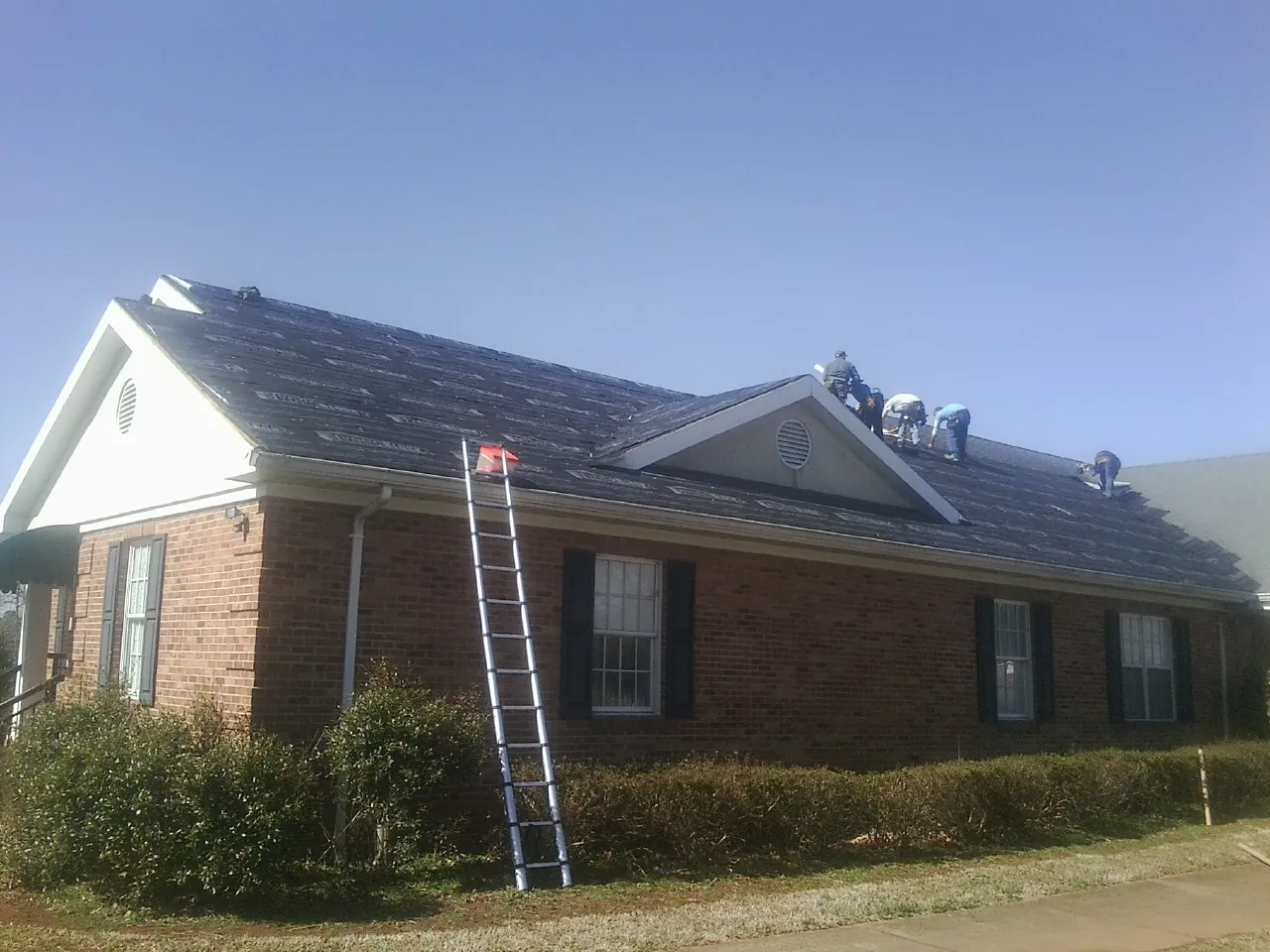 Crew tearing shingles off a brick ranch roof with a ladder set — Emergency Roof Repair work by our crew in Lyndon